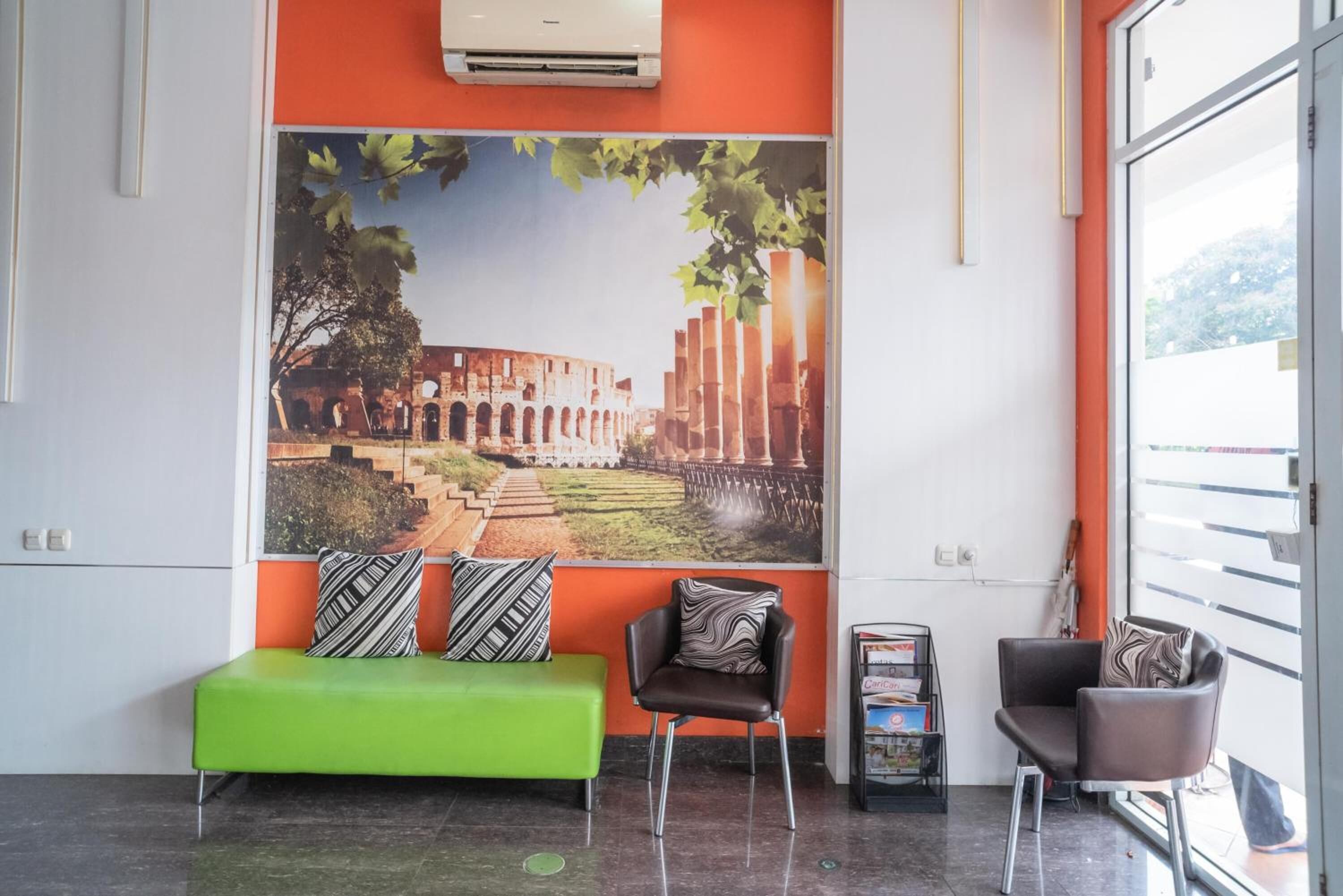A lobby with a green sofa, two armchairs, and a large mural of an ancient structure.