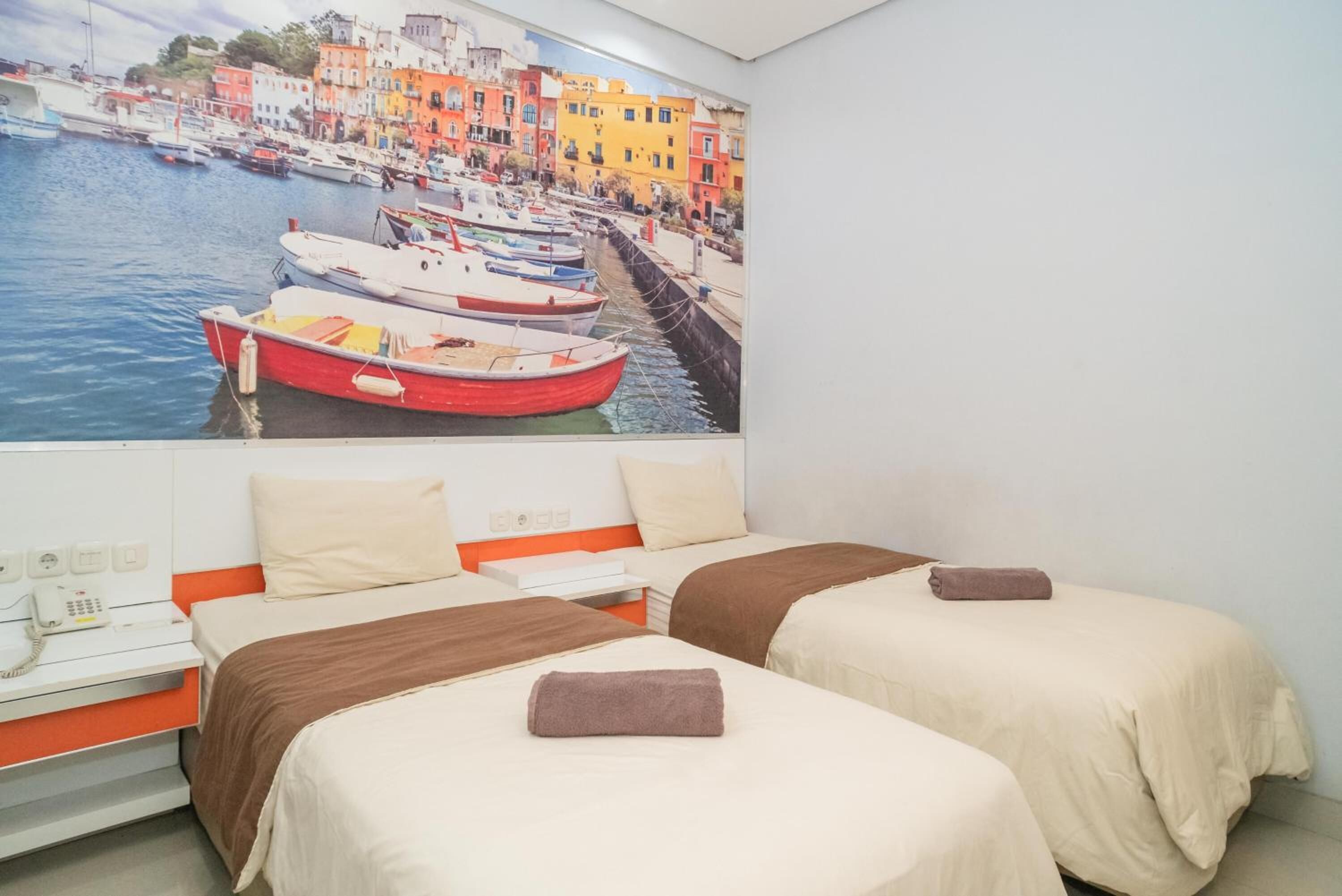 Ein Hotelzimmer mit zwei Betten, einem Hafenbild, einem Telefon und einem kleinen Schreibtisch.