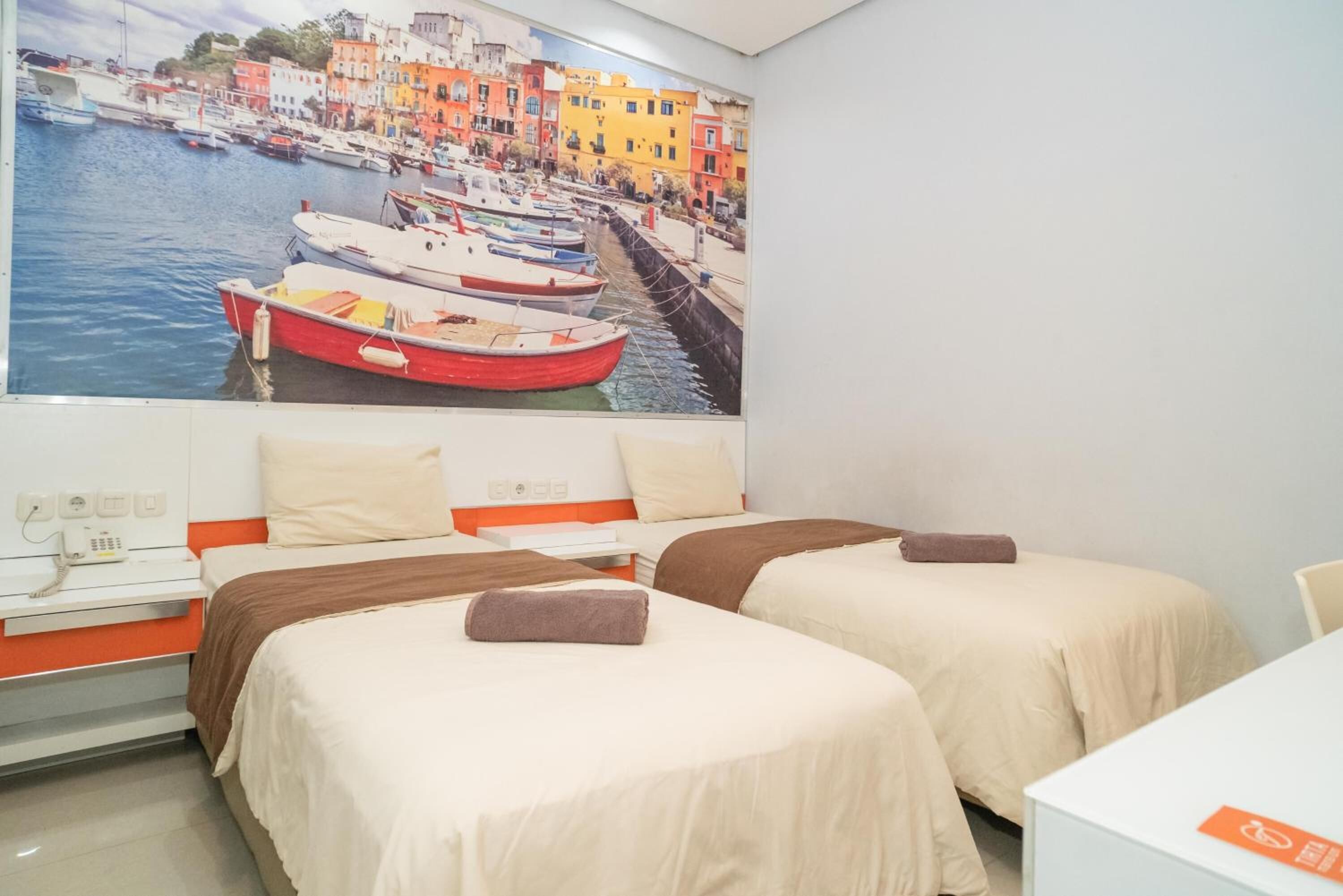 Habitación de hotel con dos camas, un gran mural de un puerto y un escritorio blanco.