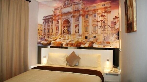 A hotel room with a large bed, a headboard, a nightstand, and a wall mural of a historical building. - Tirta Mansion Paramount Serpong Hotel (Gading Serpong)