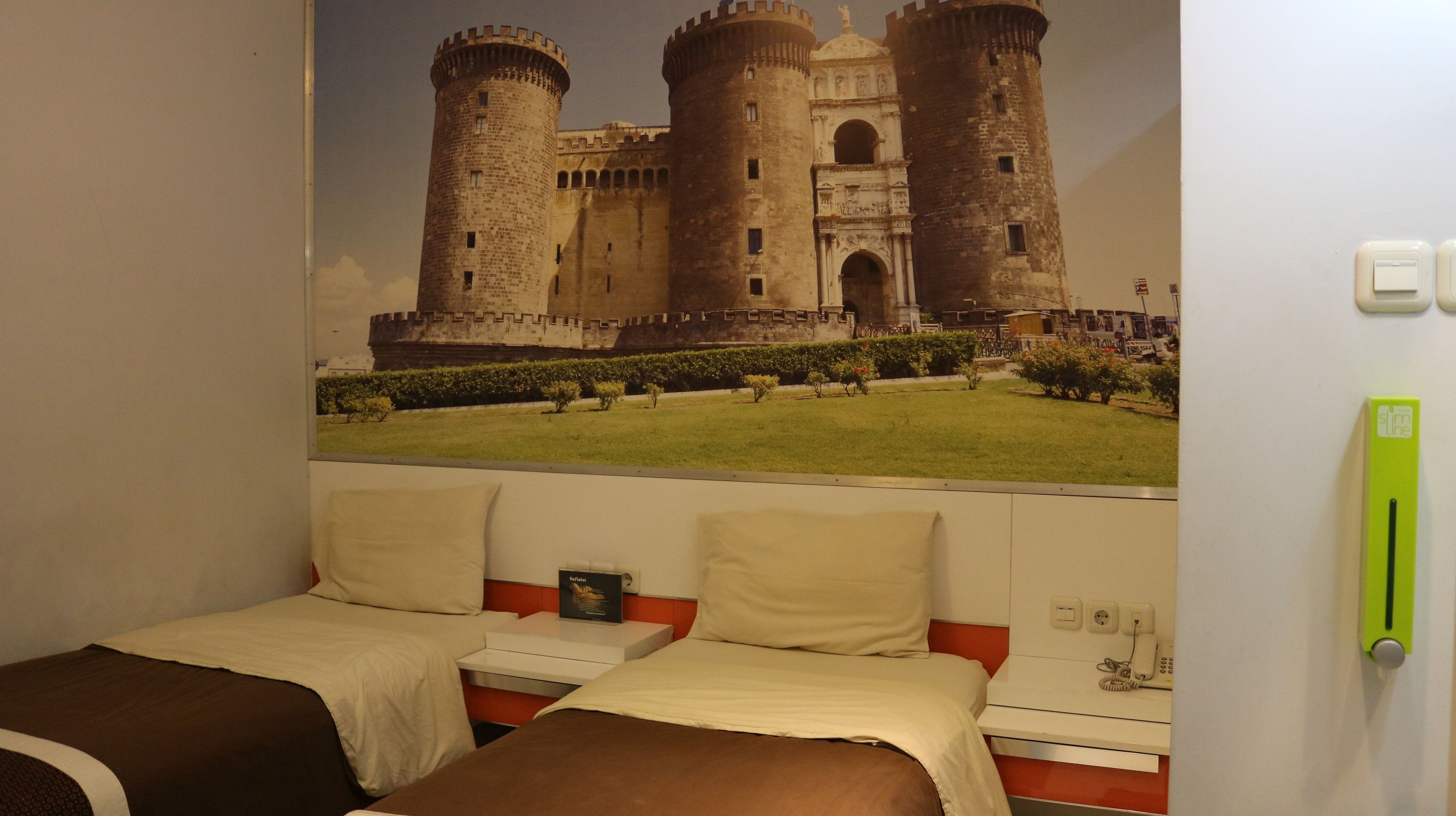 Een hotelkamer met twee bedden, een groot muurdecoratie van een kasteel en een groen nooduitgangsbord.