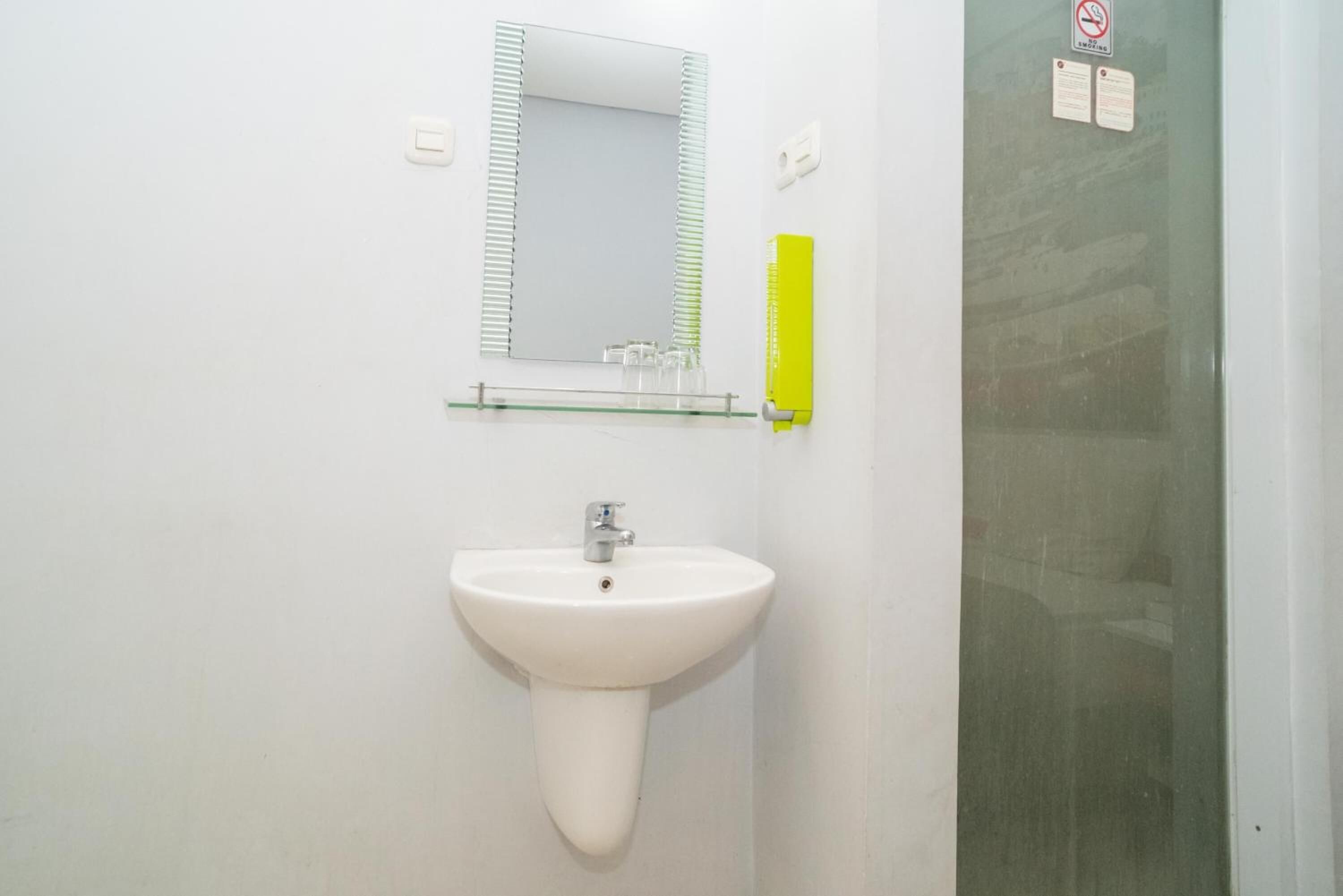 Un baño con un lavamanos blanco, un espejo y una repisa de vidrio arriba.