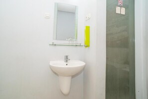 Un baño con un lavamanos blanco, un espejo y una repisa de vidrio arriba.