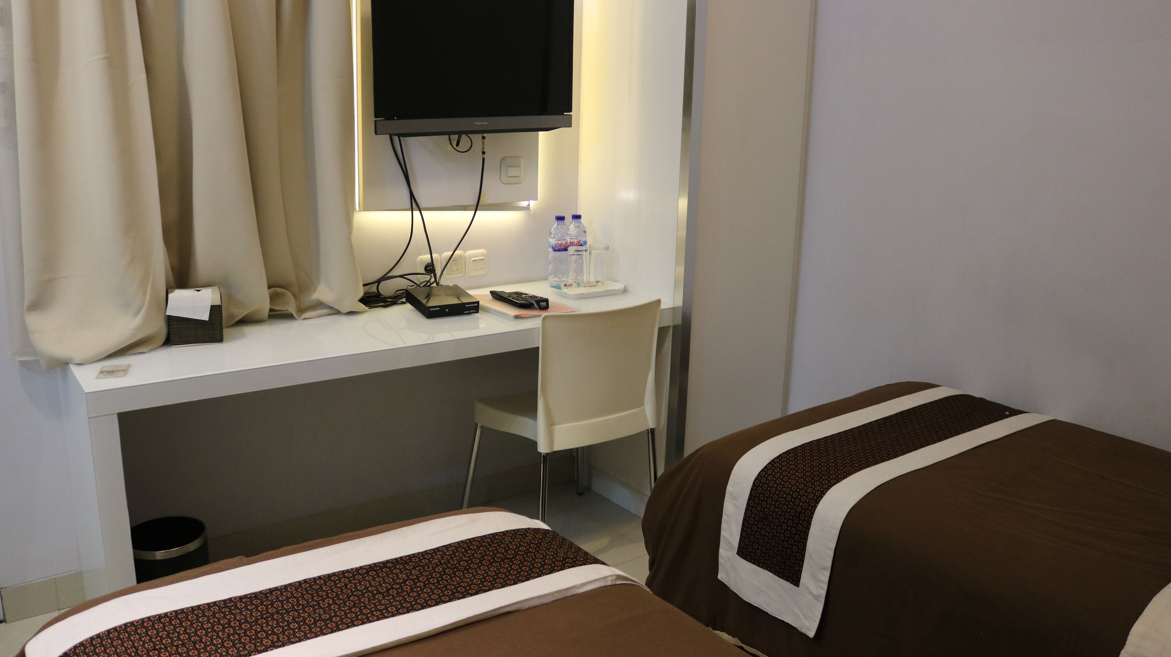 A hotel room with a desk, a TV, two beds, and a trash bin.