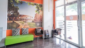A lobby with a green sofa, black chairs, and a large mural of an ancient structure. - Tirta Mansion Paramount Serpong Hotel (Gading Serpong)
