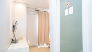 A hotel room with a white desk, a mirror, a door with a no-smoking sign, and a curtain. - Tirta Mansion Paramount Serpong Hotel (Gading Serpong)