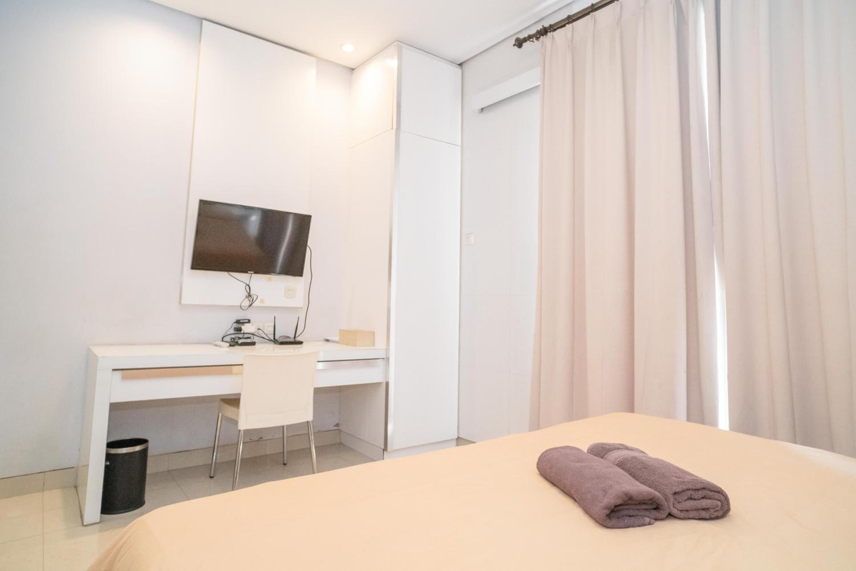 Habitación de hotel con cama, escritorio con silla, televisor montado en la pared y ventana con cortinas.