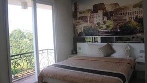 A bedroom with a large bed, a balcony with a wrought iron railing, and a mural of a historical building on the wall. - Tirta Mansion Paramount Serpong Hotel (Gading Serpong)
