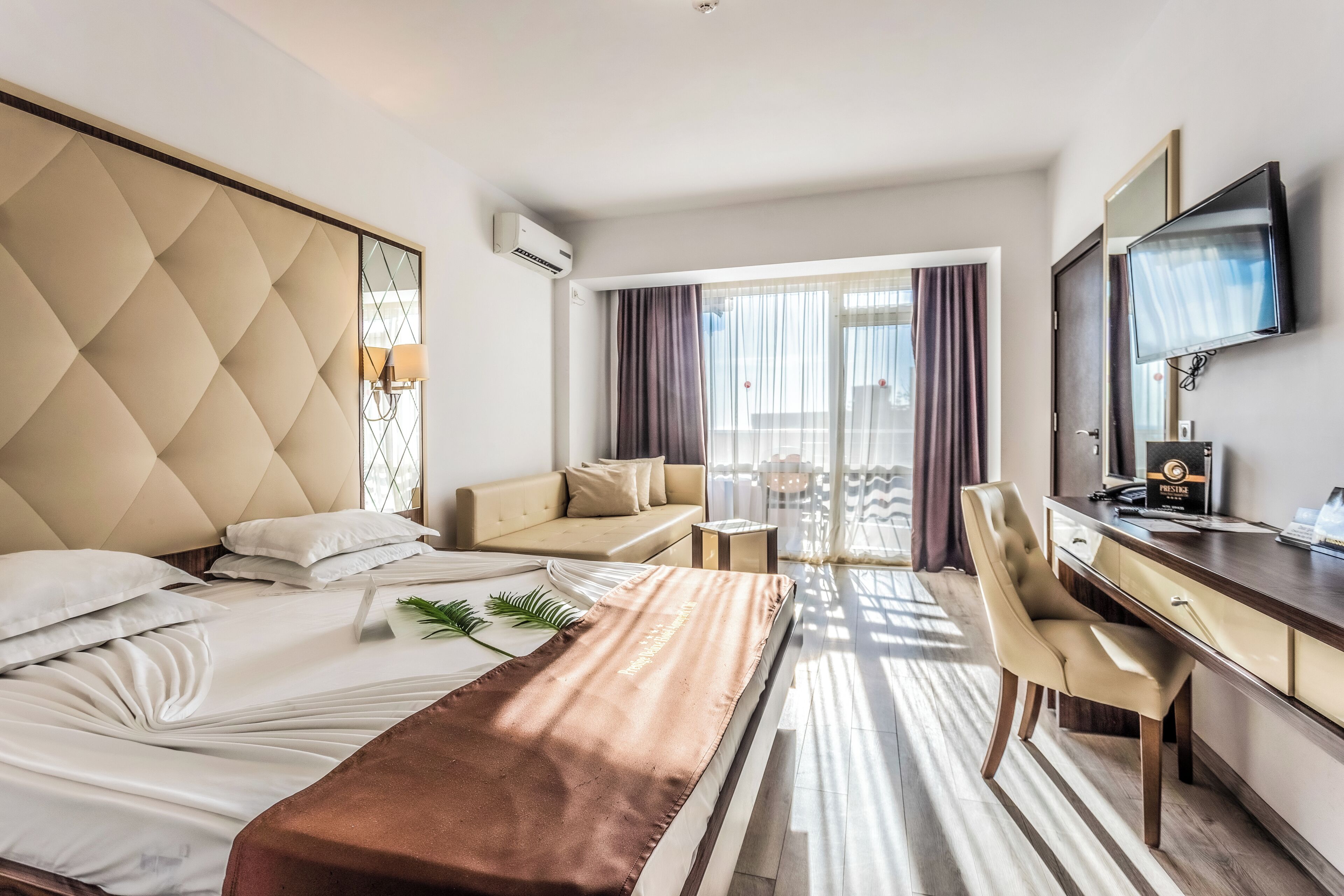 A hotel room with a bed, a desk, a chair, a TV, and a balcony with curtains.