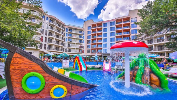 A water park with slides and a large fountain, surrounded by multi-story buildings with balconies. - Prestige Deluxe Hotel & Aquapark Club - All Inclusive (Golden Sands)