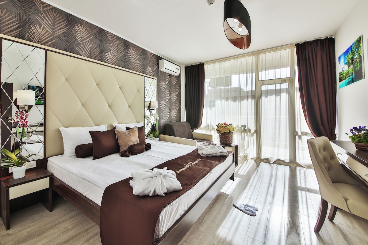 Una habitación de hotel con una cama grande, un escritorio, una silla, un espejo y una ventana con cortinas.