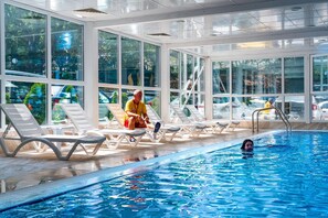An indoor swimming pool with clear glass walls, lounge chairs, and a view of the outside. - Prestige Deluxe Hotel & Aquapark Club - All Inclusive (Golden Sands)