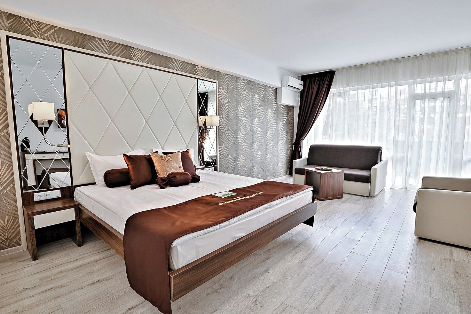 A modern hotel room with a large bed, a sofa, a small table, and a mirror.