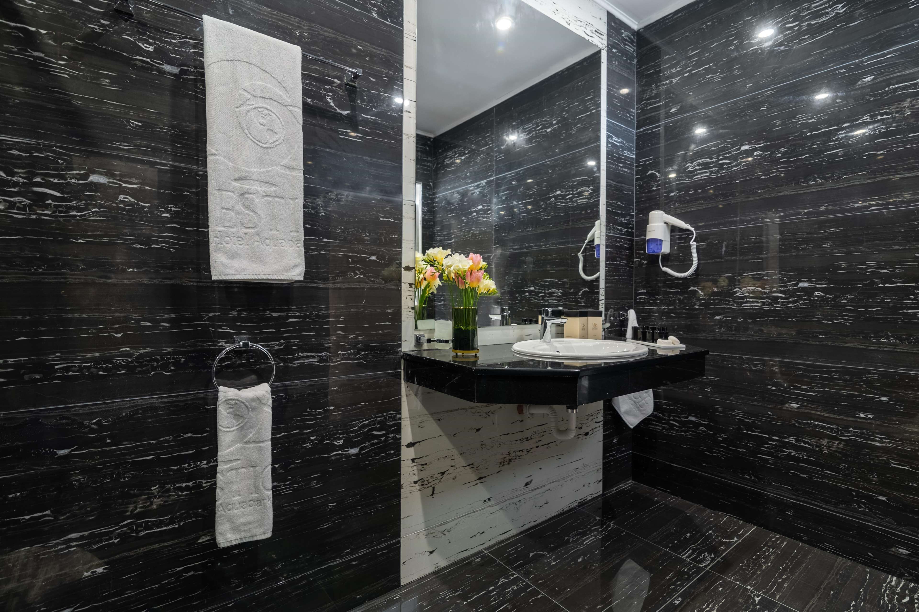 A modern bathroom with dark marble walls, a large mirror, a sink, and a towel rack.