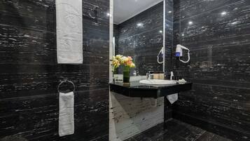 A modern bathroom with dark marble walls, a large mirror, a sink, and a towel rack.