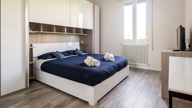 A modern bedroom with a large bed, built-in shelving, a desk, and a window.