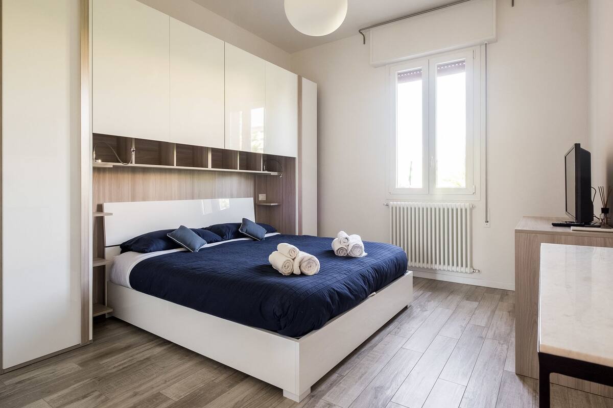 A modern bedroom with a large bed, built-in shelving, a desk, and a window.