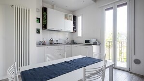 A modern kitchen with white cabinetry, a dining table with a blue table runner, and a large sliding glass door leading to a balcony.