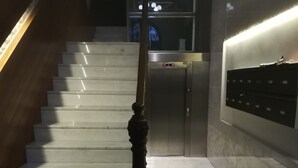 Una escalera con barandilla de madera y un indicador digital de ascensor.