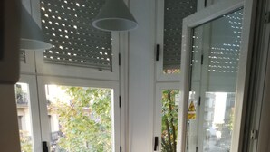 Una habitación con un asiento junto a la ventana, una mesita con una planta y una silla con un cojín estampado.