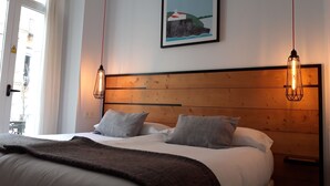 Un dormitorio con cabecera de madera, dos lámparas de noche, una cama con ropa de cama blanca y almohadas grises, y un cuadro en la pared.
