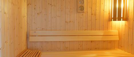 Una sauna con paredes y bancos de madera, un cubo con una cuchara, y un termómetro en la pared.