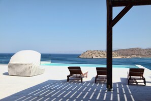 Zona de piscina con sillones de descanso y un espacio de estar cubierto con vistas al mar.