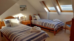 A cozy attic bedroom with two beds, a wooden headboard, a nightstand, a lamp, and a view of the sea through skylights. - Gowan Bank (Montrose)
