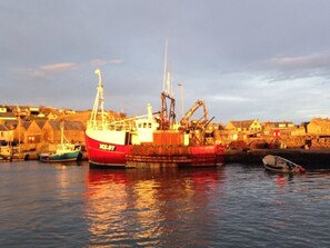 A harbor with a large red fishing boat docked, smaller boats, and a calm water setting. - Gowan Bank (Montrose)