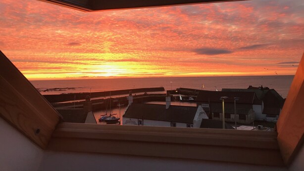 A sunset view from a window overlooking a harbor with boats and buildings. - Gowan Bank (Montrose)