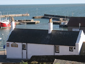 A coastal building with a white facade and a black roof, situated near a harbor with boats and a pier. - Gowan Bank (Montrose)
