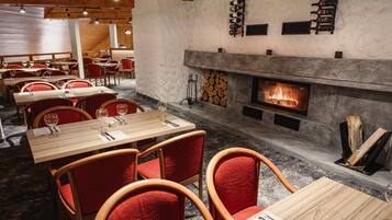 A restaurant interior with wooden tables and red chairs, a fireplace with logs, and a wine rack on the wall.