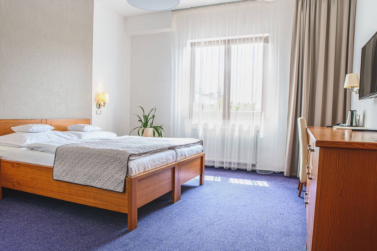 A hotel room with a wooden bed, a desk, a chair, a TV, and a window with curtains.