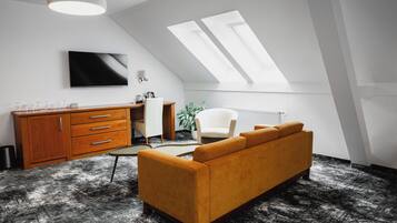 A modern loft bedroom with a sloped ceiling, skylights, a large bed, a sofa, a desk, and a TV.
