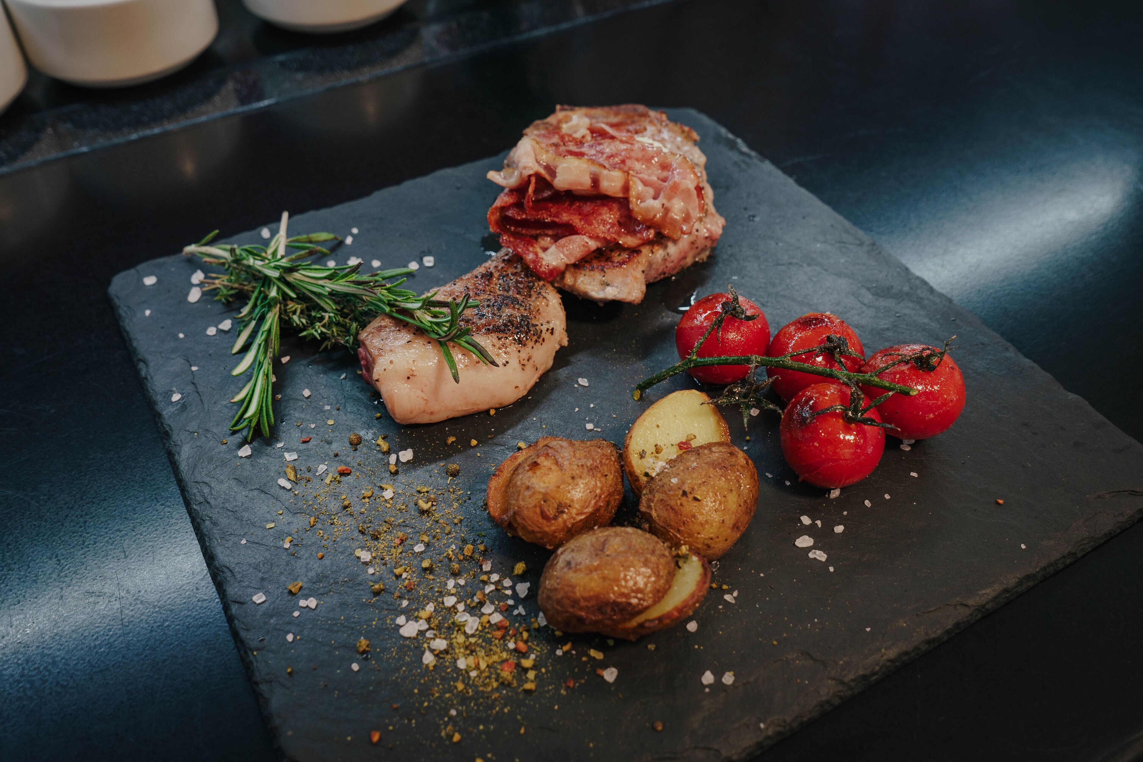 Una tabla de pizarra con un trozo de carne a la parrilla, patatas asadas y tomates cherry.