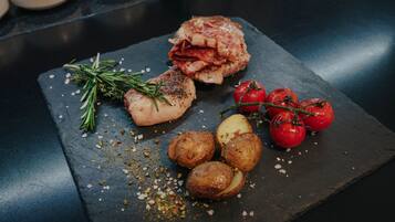 Una tabla de pizarra con un trozo de carne a la parrilla, patatas asadas y tomates cherry.