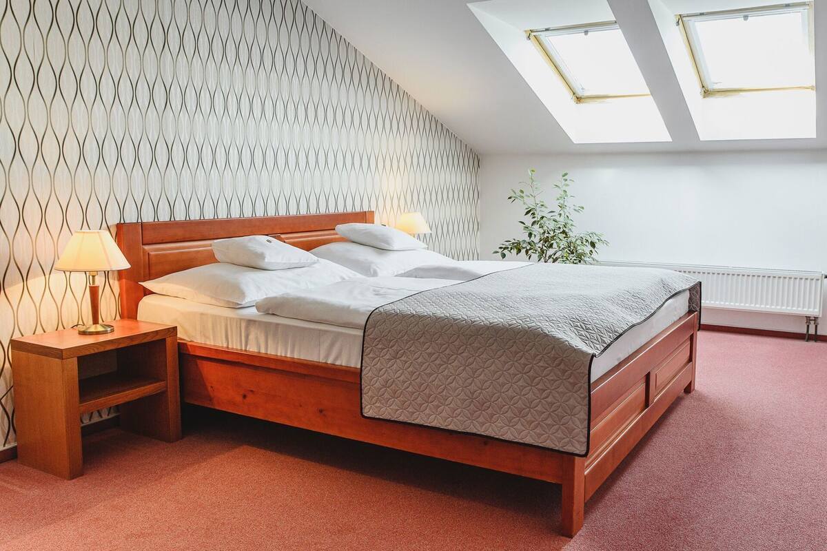 A bedroom with a wooden bed, a nightstand, a lamp, a radiator, and a plant.