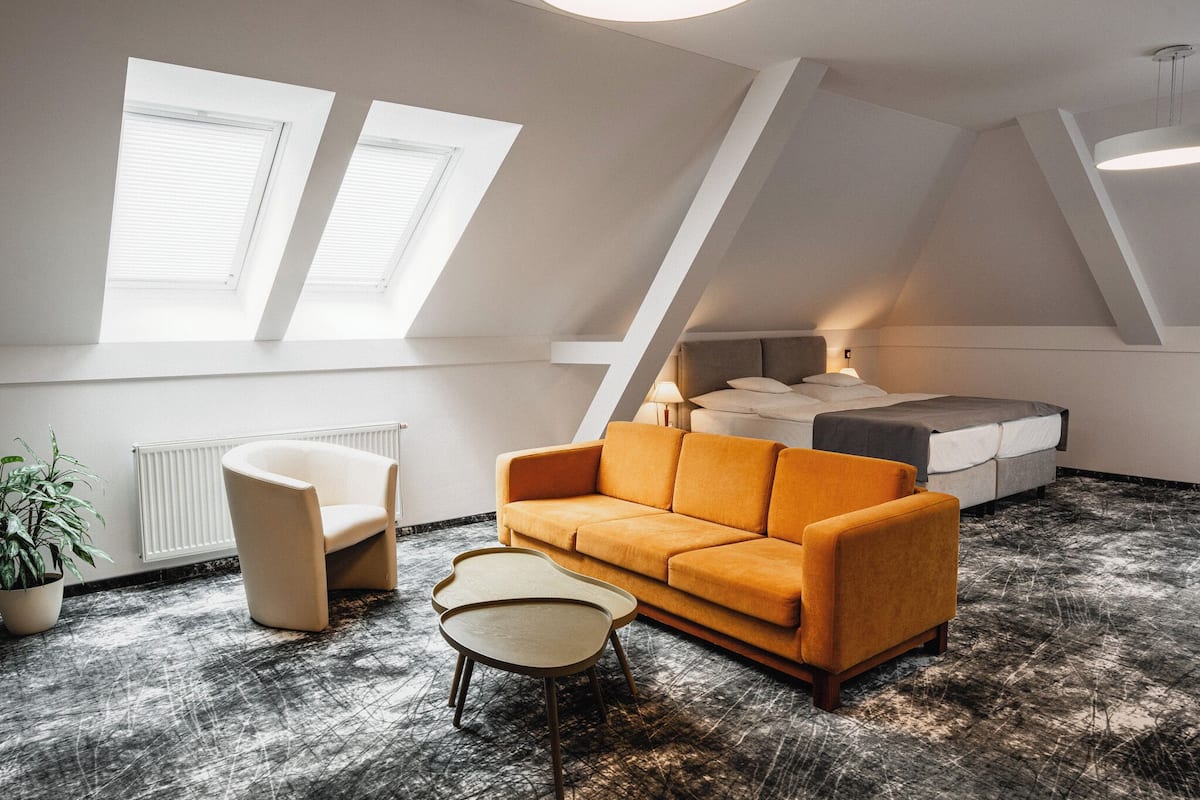 A modern loft bedroom with a sloped ceiling, a sofa, a bed, and a small table.