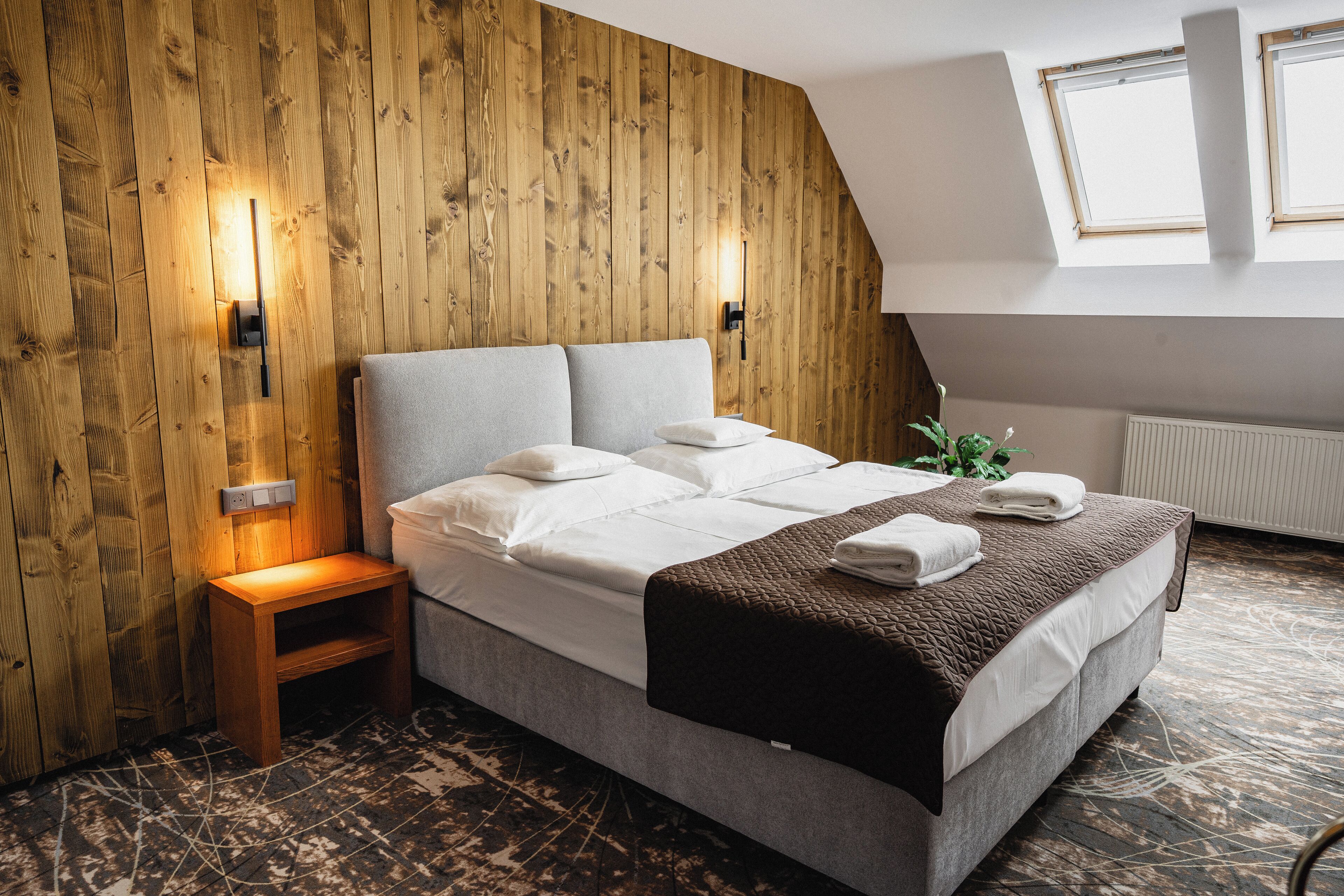Un dormitorio con pared de madera, una cama con ropa blanca, una mesita de noche de madera y un radiador.
