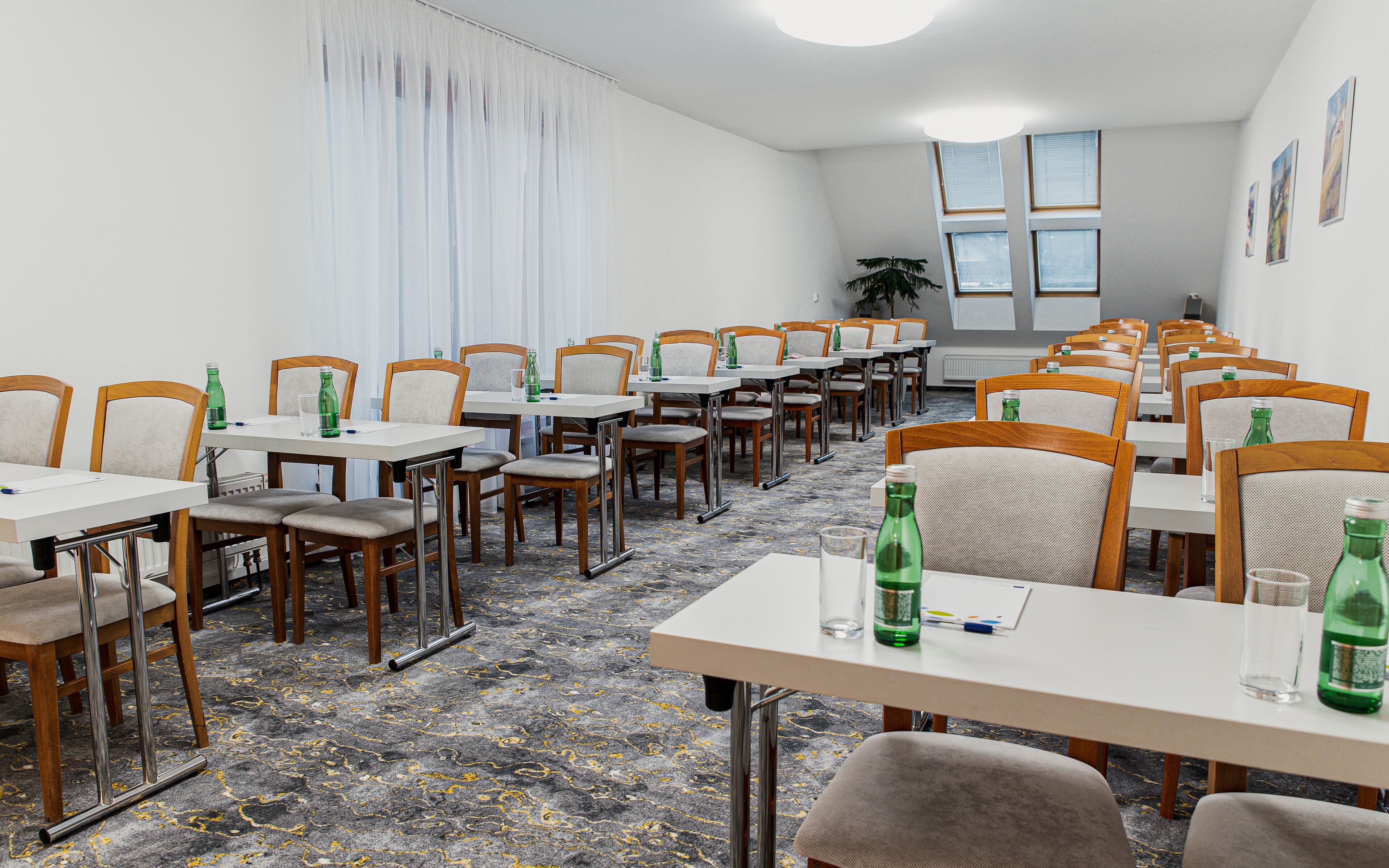 A conference room with rows of tables and chairs, white walls, and large windows.