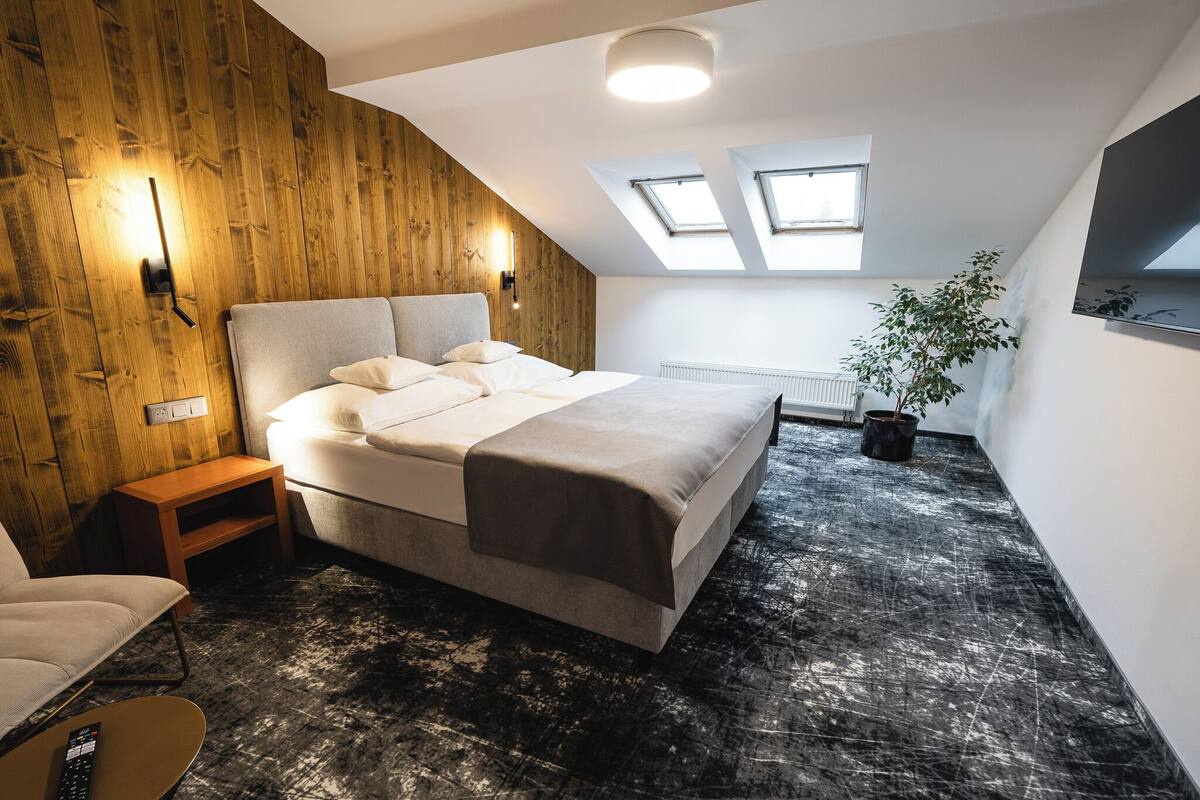 A bedroom with a large bed, wooden wall paneling, skylights, a potted plant, and a radiator.