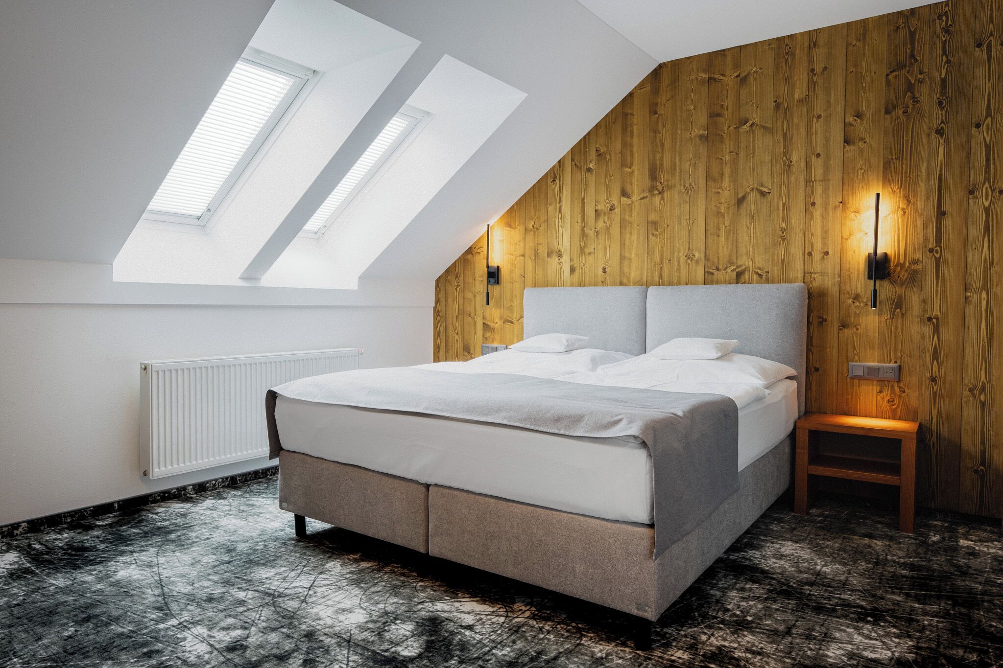 A bedroom with a sloped ceiling, skylights, a bed, a nightstand, and a wooden wall panel.