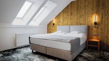 A bedroom with a sloped ceiling, skylights, a bed, a nightstand, and a wooden wall panel.