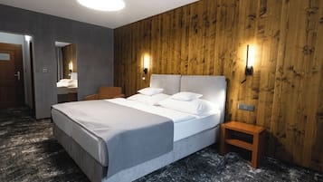 Una habitación de hotel moderna con una cama grande, paneles de madera y una mesita de noche pequeña de madera.