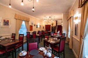 Un área de comedor con varias mesas y sillas, un candelabro y una escalera que conduce a otro nivel.