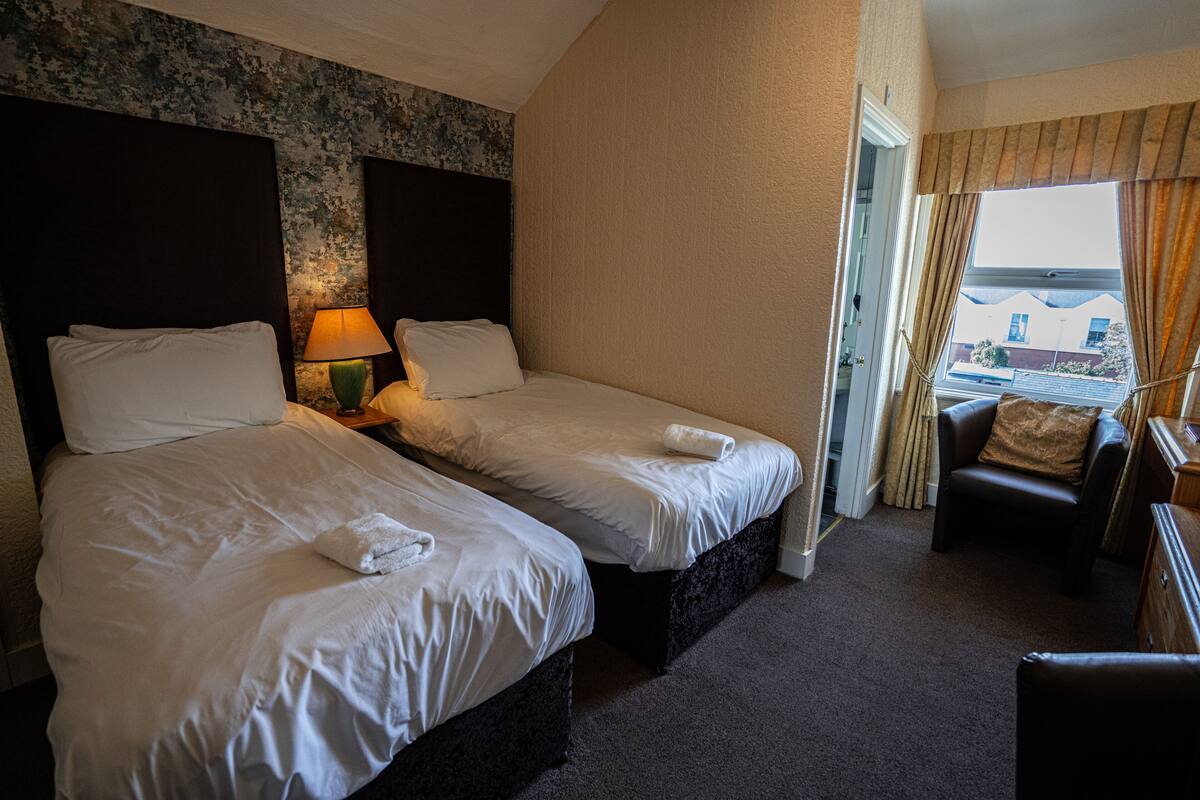 A hotel room with two beds, a sitting area with a chair, and a view through a window.