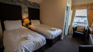 A hotel room with two beds, a sitting area with a chair, and a view through a window.