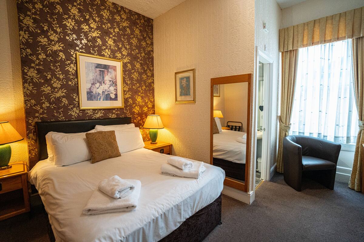 A hotel room with a large bed, two bedside lamps, a chair, a mirror, and a window with curtains.