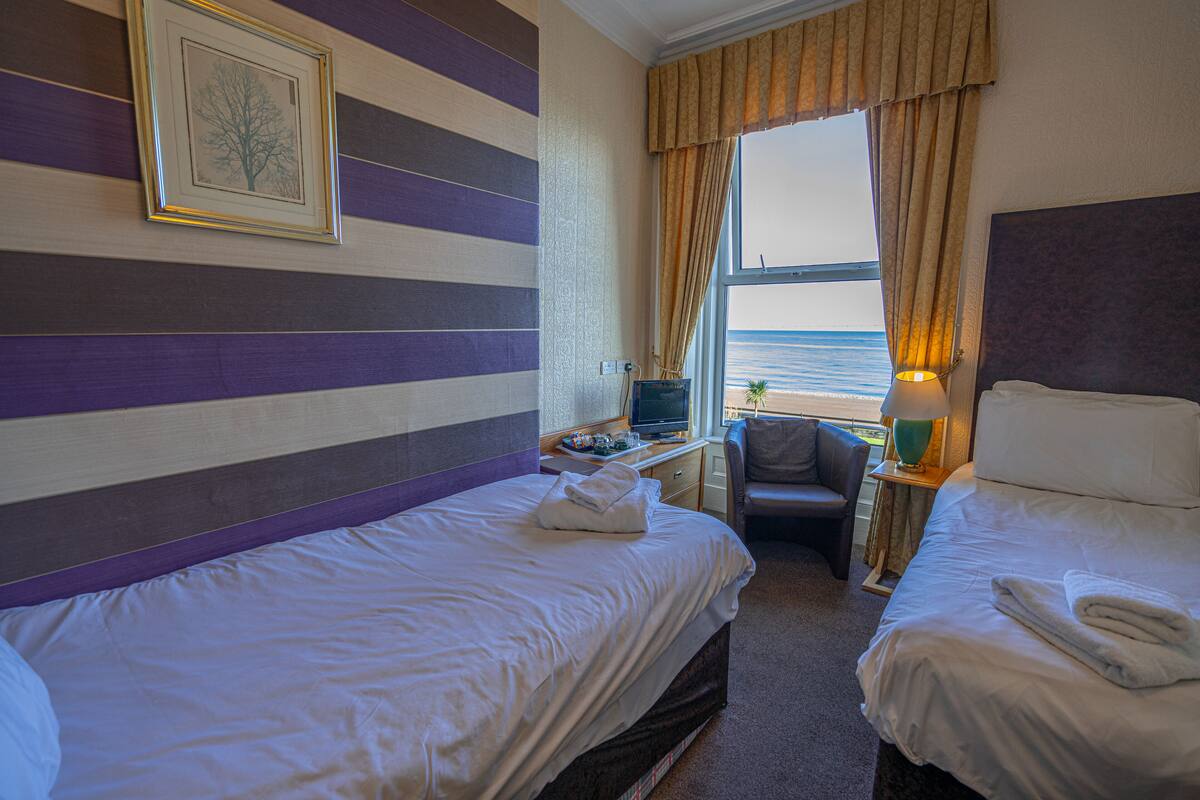 A hotel room with two beds, a desk with a computer, a chair, and a view of the sea.