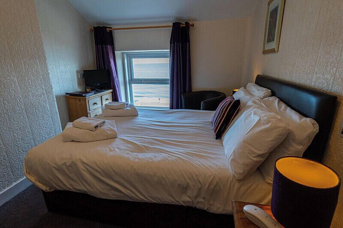 A hotel room with a large bed, a desk with a television, and a window with curtains.